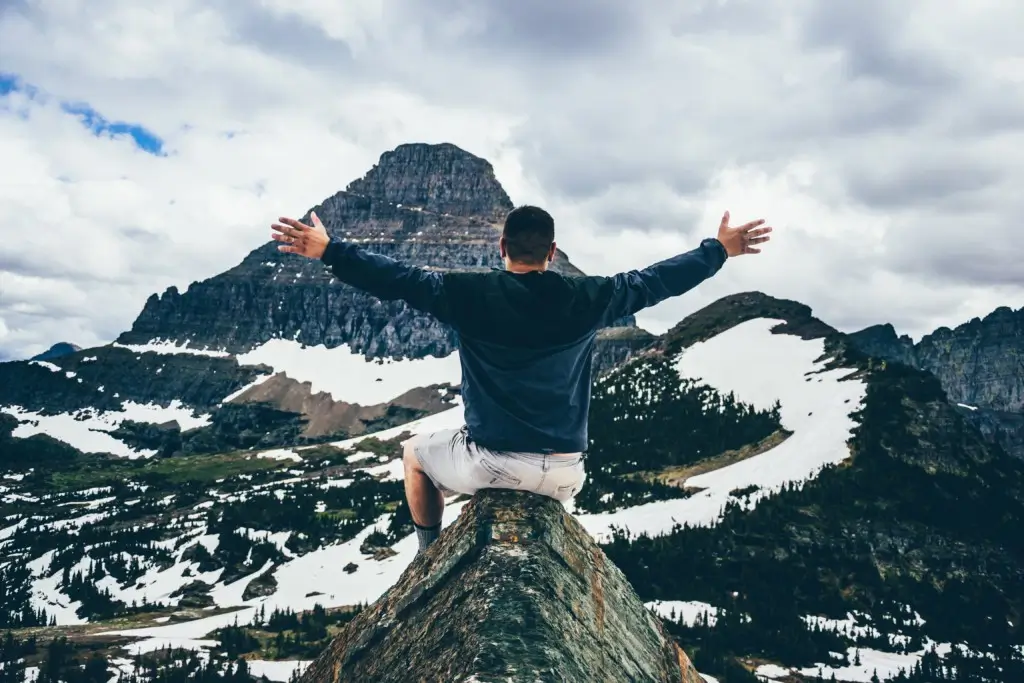 Man spreads his arms wide as he sits on top a mountain