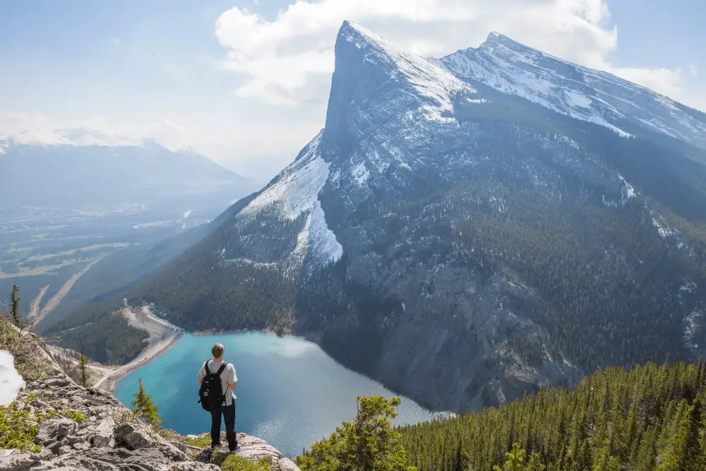 hiker standing across from glacier lake and towering mountain