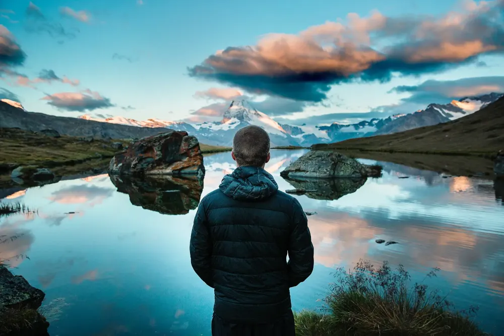 Man stares across a glacier lake at a snowy peak
