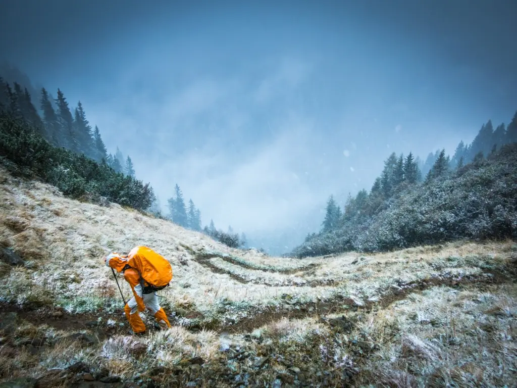 Hiker navigates across snow dusted field along mountain pass.